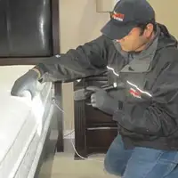 Bed bug inspection technician checking a mattress and bed frame for signs of infestation in Huntsville, AL