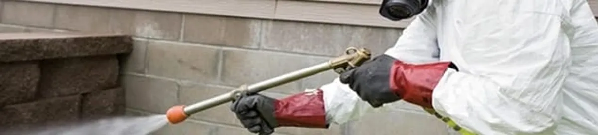 Pest control technician applying exterior insect treatment along a home foundation in Huntsville, AL