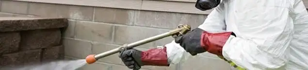 Pest control technician applying exterior insect treatment along a home foundation in Huntsville, AL