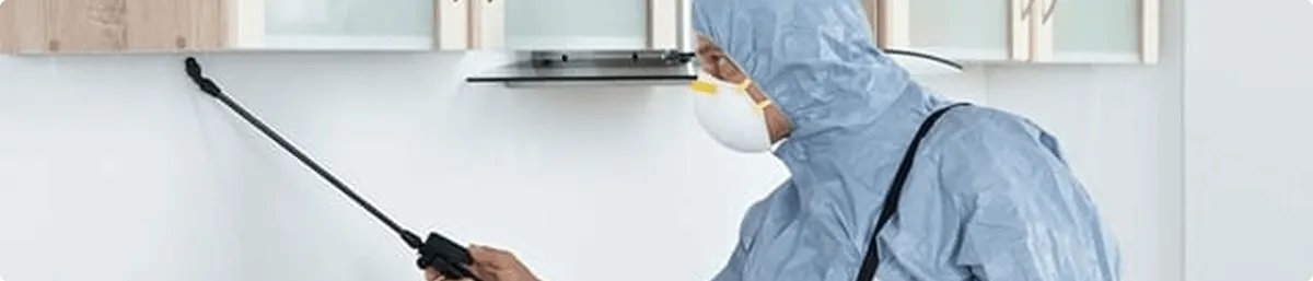 Pest control technician spraying along baseboards for indoor pest treatment in Huntsville, AL
