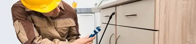 Roach exterminator applying treatment under kitchen cabinets in Huntsville, AL