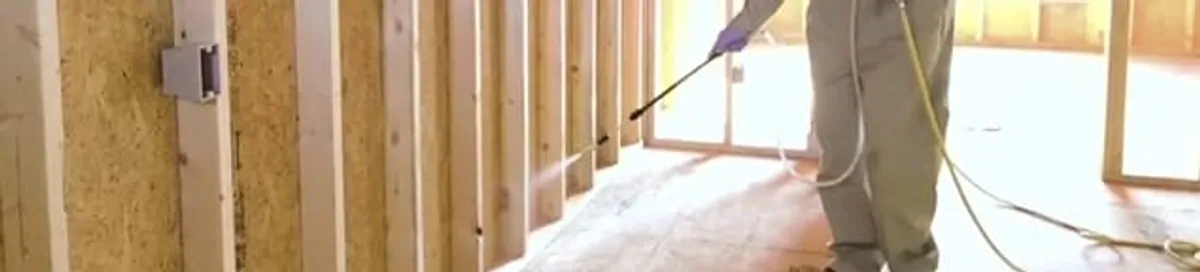 Termite treatment technician applying spray along framing and unfinished walls in Huntsville, AL