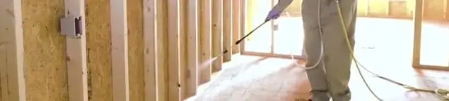 Termite treatment technician applying spray along framing and unfinished walls in Huntsville, AL